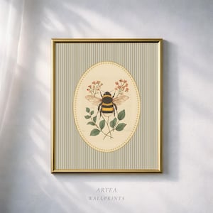 May include: Framed wall art print with a bee illustration. The bee, with yellow and black stripes, is surrounded by red flowers and green leaves, set against a striped background. The gold frame surrounds the artwork. The text "ARTEA WALLPRINTS" is at the bottom.