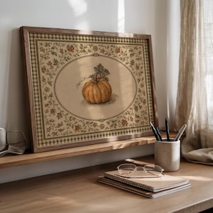 May include: A rectangular framed print featuring a central illustration of an orange pumpkin inside an oval border. The surrounding area displays a detailed floral pattern with green leaves and small red flowers, finished with a green gingham border.