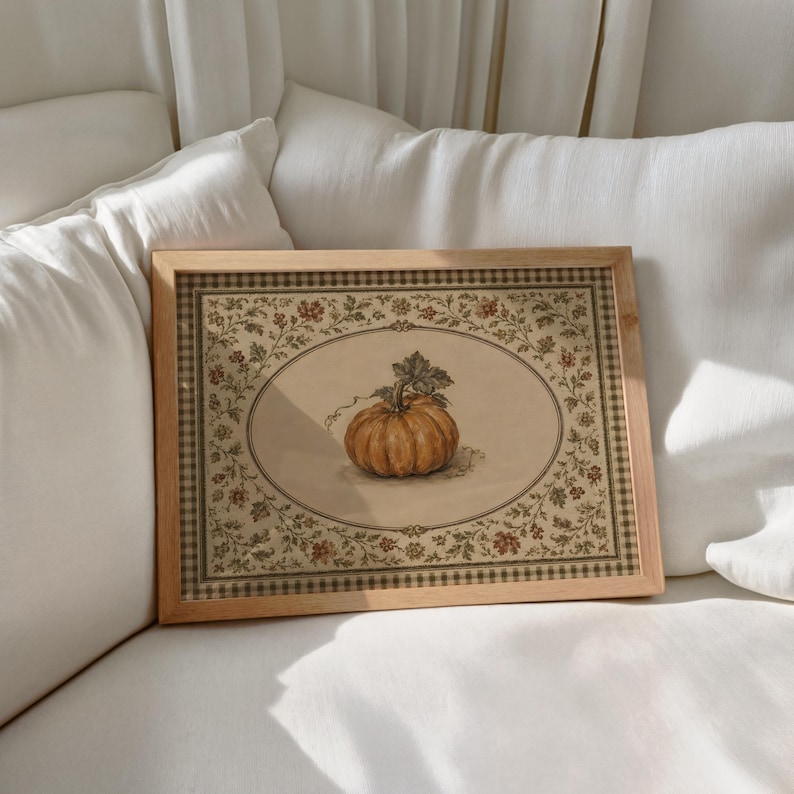 May include: A rectangular wooden frame containing a print of a single orange pumpkin centered within an oval border. The print features a detailed floral vine pattern surrounding the oval and a checkered border edge in muted earth tones.