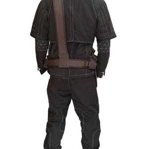 Puede incluir: Mono negro con costuras blancas, con una chaqueta de manga corta y pantalones a juego. El conjunto incluye una correa para el hombro y un cintur&oacute;n marrones. Se ven patrones geom&eacute;tricos en las mangas. El dise&ntilde;o sugiere un tema t&aacute;ctico o militar.