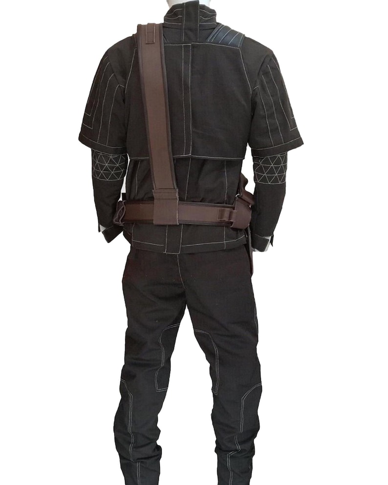 Puede incluir: Mono negro con costuras blancas, con una chaqueta de manga corta y pantalones a juego. El conjunto incluye una correa para el hombro y un cintur&oacute;n marrones. Se ven patrones geom&eacute;tricos en las mangas. El dise&ntilde;o sugiere un tema t&aacute;ctico o militar.