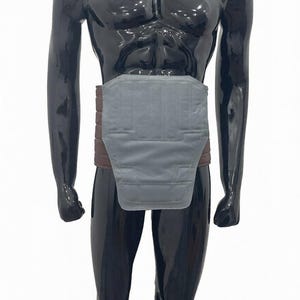 Puede incluir: Un cintur&oacute;n de soporte lumbar gris y marr&oacute;n se muestra en un maniqu&iacute; negro. El cintur&oacute;n presenta una secci&oacute;n gris acolchada y una banda marr&oacute;n. El maniqu&iacute; est&aacute; colocado sobre un fondo blanco.