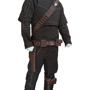 Puede incluir: Un disfraz marr&oacute;n oscuro con cuello alto, hombreras y cintur&oacute;n utilitario. El disfraz incluye una funda, una armadura para las piernas y una bandolera. Las costuras blancas acent&uacute;an las mangas y los pantalones. El atuendo se muestra en un maniqu&iacute;.