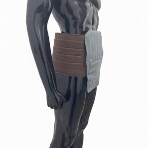 Puede incluir: Una faja de soporte abdominal marr&oacute;n y gris. La faja est&aacute; hecha de un material suave y acolchado y presenta una secci&oacute;n marr&oacute;n acanalada que se envuelve alrededor de la cintura. Una secci&oacute;n rectangular gris est&aacute; unida en la parte delantera.