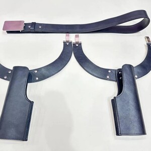 May include: A black leather belt with a silver buckle and two matching black leather holsters. The holsters are attached to curved black leather supports with silver hardware. The items are displayed on a white surface.