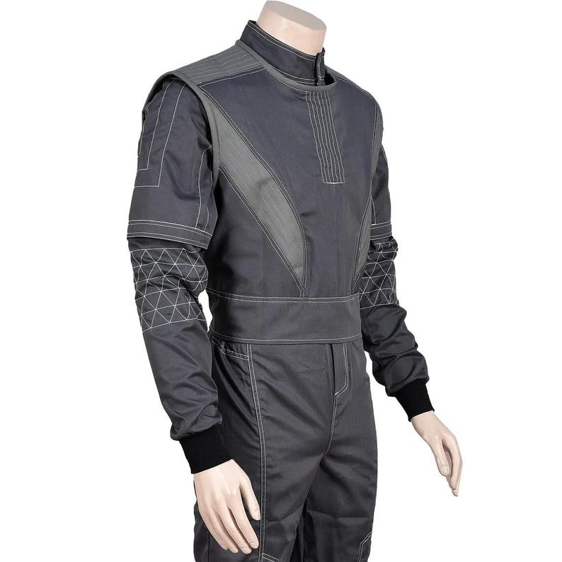 Puede incluir: Traje de carreras gris oscuro con detalles en gris claro y costuras blancas. El traje presenta un cuello alto, mangas largas y cintura entallada. Patrones geom&eacute;tricos adornan los brazos y los pu&ntilde;os son negros.