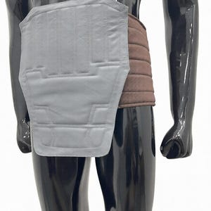 Puede incluir: Un protector de espalda de cuero gris con costuras verticales y un cintur&oacute;n acolchado marr&oacute;n. El protector de espalda es rectangular con un borde inferior curvo. El maniqu&iacute; es negro.