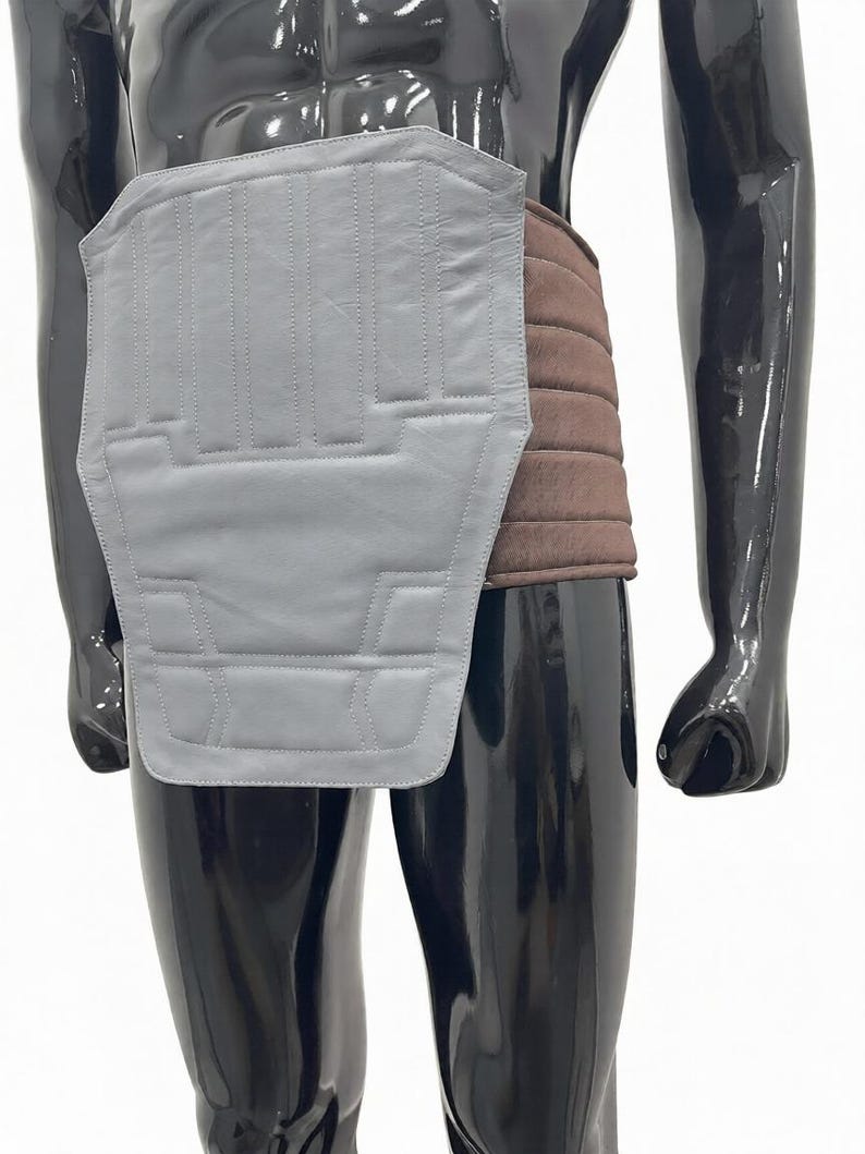 Puede incluir: Un protector de espalda de cuero gris con costuras verticales y un cintur&oacute;n acolchado marr&oacute;n. El protector de espalda es rectangular con un borde inferior curvo. El maniqu&iacute; es negro.