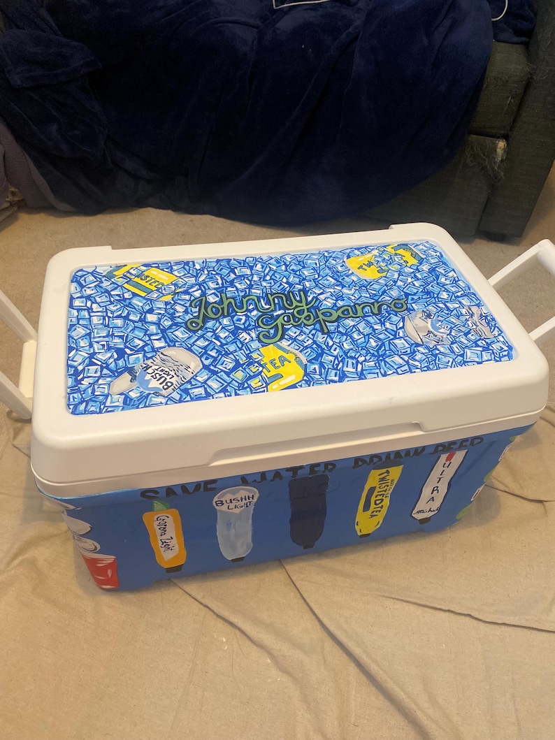 May include: A white and blue cooler with a hand-painted design. The lid features a blue background with ice cubes and the text "Johnny Gapparo Tea". The cooler's side has painted beverage logos.