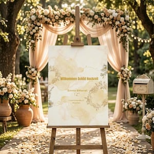 Könnte beinhalten: Eine hölzerne Staffelei zeigt ein Hochzeits-Willkommensschild mit dem Text "Willkommen Schild Hochzeit" und den Namen "Emma & Marcel". Das Schild hat ein Aquarelldesign mit floralen Akzenten. Die Szene ist im Freien mit Blumendekorationen.