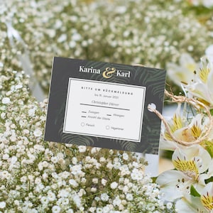 Könnte beinhalten: Eine Hochzeitseinladungskarte mit den Namen "Karina & Karl" in goldfarbenen Buchstaben, umgeben von weißen Blumen und Grün. Die Karte enthält Text und Platz für eine Antwort.