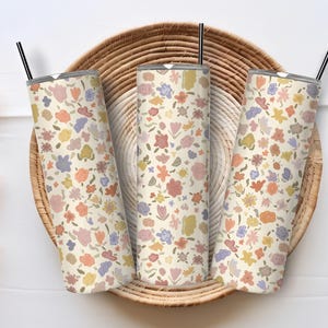 May include: Three stainless steel tumblers featuring a floral design in shades of pink, yellow, and blue. The tumblers are displayed in a woven basket.