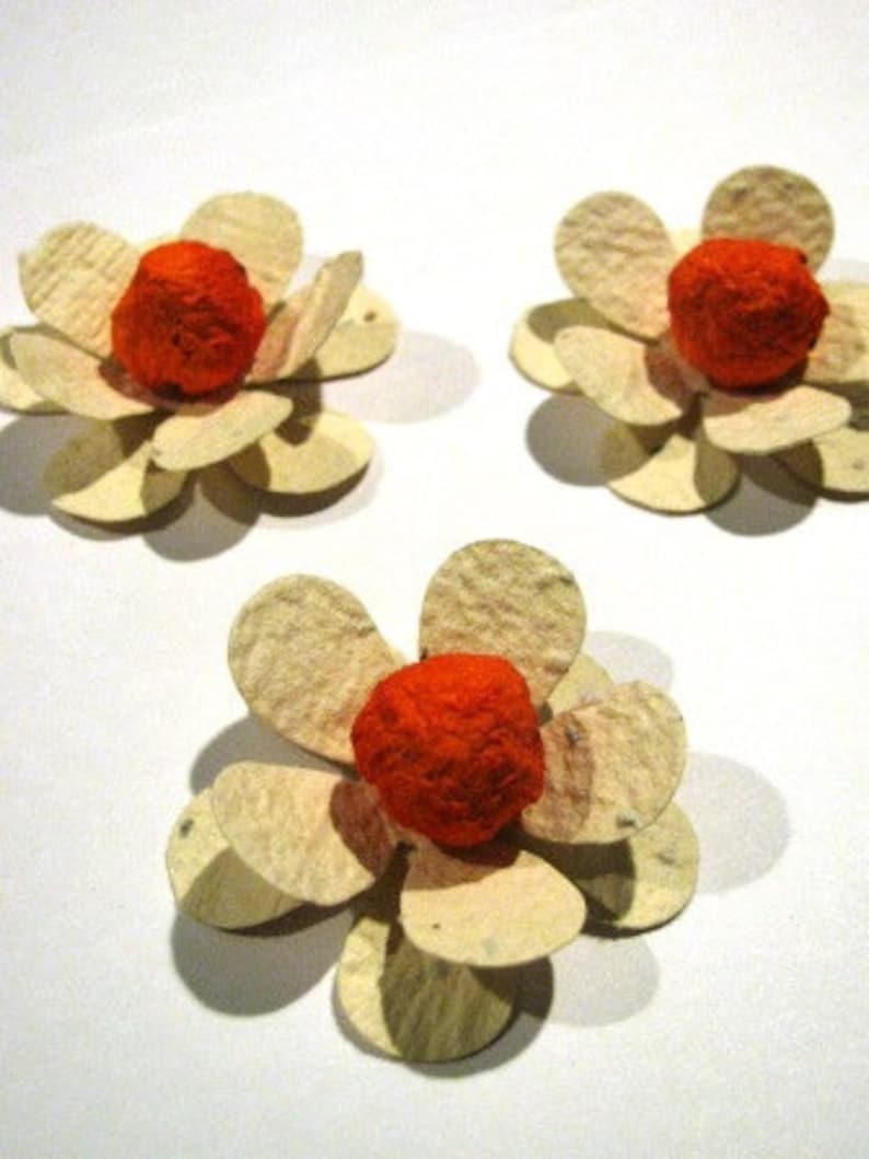 K&ouml;nnte beinhalten: Drei Papierblumen mit orangenen Zentren und wei&szlig;en Bl&uuml;tenbl&auml;ttern. Die Blumen sind aus Recyclingpapier hergestellt und eine gro&szlig;artige M&ouml;glichkeit, Ihrem Zuhause einen Hauch von Farbe zu verleihen.