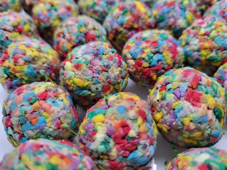 May include: Close-up of colorful, textured seed balls. Each ball is made of recycled paper and contains a variety of wildflower seeds.