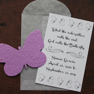 May include: A white card with a butterfly design and the text "What the caterpillar calls the end, God calls the Butterfly" and "Susan Garcia April 25, 1945 to September 23, 2018". A purple butterfly-shaped seed paper is in the background.