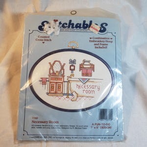 May include: A cross-stitch kit featuring a bathroom scene with the words "necessary room." The kit includes a flexible hoop and embroidery thread. The design measures 7" x 5".