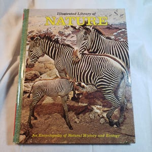 May include: A hardcover book titled "Illustrated Library of NATURE" featuring a cover image of three zebras. The book's subtitle reads "An Encyclopedia of Natural History and Ecology". The spine is green with red accents.