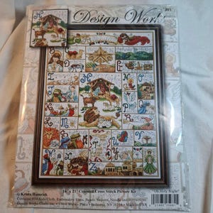 May include: A Design Works counted cross stitch picture kit titled Oh Holy Night. The packaging features a colorful alphabet sampler design with religious nativity scenes, animals, and angels. It includes 16 x 21 inch Aida cloth, floss, and beads.