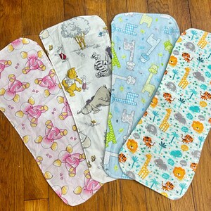 May include: Four baby burp cloths with different patterns. One is pink with elephants, another features Winnie the Pooh characters, a third has giraffes, and the last has lions and tigers. The cloths are made of soft fabric.
