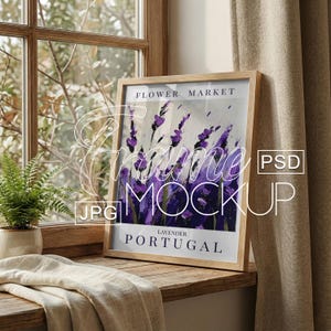 May include: A framed art print featuring a lavender field painting with the text "Flower Market Lavender Portugal." The artwork is in a light wooden frame, displayed on a wooden windowsill with a fern and a beige curtain in the background.