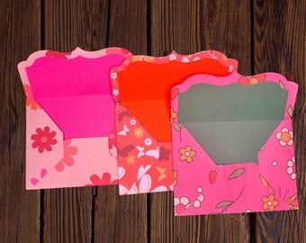 May include: Three pink envelopes with floral patterns and scalloped edges. The envelopes are folded open to reveal a pink, orange, and green interior.