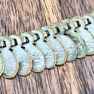 May include: A silver and gold chain necklace made of linked coin-shaped charms. The charms are slightly worn and have a patina finish.
