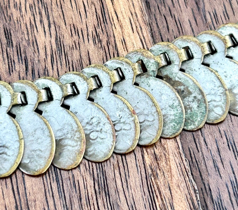 May include: A silver and gold chain necklace made of linked coin-shaped charms. The charms are slightly worn and have a patina finish.