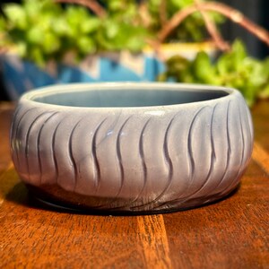 Könnte beinhalten: Eine hellgraue Keramikschale mit einem wellenförmigen, strukturierten Design. Die Schale ist rund und hat eine glatte, glänzende Oberfläche.