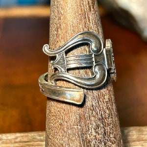 May include: A silver ring with a lyre design. The ring is on a wooden ring holder.