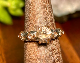 May include: A silver ring with a large, clear, faceted gemstone surrounded by smaller gemstones. The ring has a textured band.