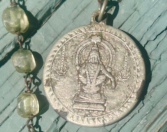 May include: A silver-toned circular pendant featuring a relief of a seated figure, suspended from a chain of translucent, pale green, irregularly shaped beads connected by thin copper-colored wire links in a rustic, handcrafted style.