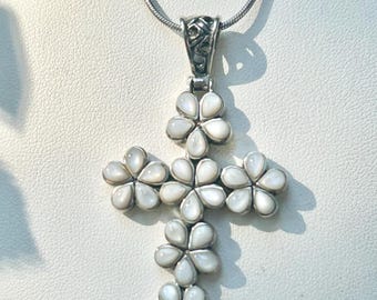 May include: A silver-toned cross pendant necklace featuring a floral design. The cross is adorned with white, petal-shaped elements, creating a flower-like appearance. The necklace has a delicate chain.