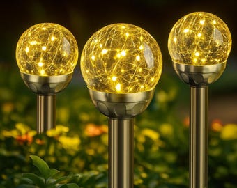 May include: Three solar-powered garden lights with a spherical glass design. Each light features a warm yellow glow from internal LEDs, encased in a cracked glass globe. The lights are mounted on bronze-colored metal poles, creating a decorative outdoor lighting display.