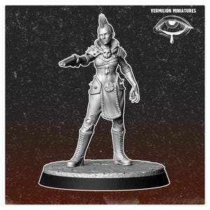May include: A grey miniature figurine of a female warrior with a mohawk hairstyle, holding a gun. The figure is wearing armour with a skull design and tall boots. The base is round and black. The text "VERMILION MINIATURES" is visible.
