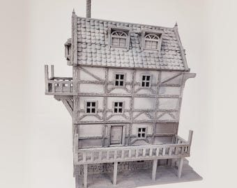 May include: A white, three-story, miniature building with a gabled roof, multiple windows, and a balcony on the second floor. The building has a wooden frame and is made of a textured material.