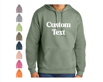 May include: A sage green hooded sweatshirt with the words "Custom Text" in white block letters. The sweatshirt has a front pocket and a drawstring hood. A variety of other colored hoodies are shown to the left of the main image.