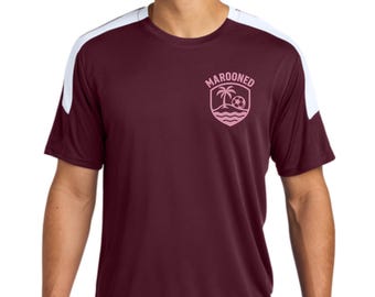 May include: Maroon athletic t-shirt with white shoulder accents. The shirt features a pink logo with the word "MAROONED" above a palm tree, soccer ball, and waves design. The shirt is made of a moisture-wicking material.