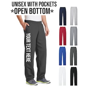 May include: Dark gray sweatpants with pockets and an open bottom. The text "YOUR TEXT HERE" is printed vertically on the left leg. The image also shows examples of sweatpants in navy, gray, red, blue, white, and black.