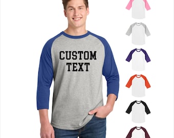 May include: A gray raglan baseball shirt with blue sleeves and the text "CUSTOM TEXT" in black block letters. The image also shows several color options for the shirt, including pink, gray, purple, orange, black, and maroon.