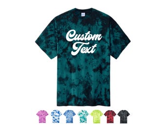 May include: A tie-dye t-shirt in shades of teal and black, with the words "Custom Text" in white script across the front. Below the shirt are several other t-shirts in various colors, including pink, blue, green, yellow, red, and black.