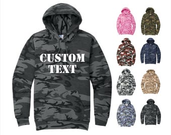 May include: A gray camouflage hoodie with the text "CUSTOM TEXT" in white. The image also shows eight other hoodies in various camouflage patterns and colors, including pink, green, and blue.