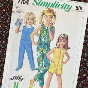 May include: A vintage Simplicity sewing pattern, number 7154, for girls' clothing, size 8. The pattern shows illustrations of girls in jumpsuits and a romper. Designs include a blue jumpsuit, a floral jumpsuit, and a yellow romper. The pattern is marked "Jiffy" and "easy cut - easy sew".