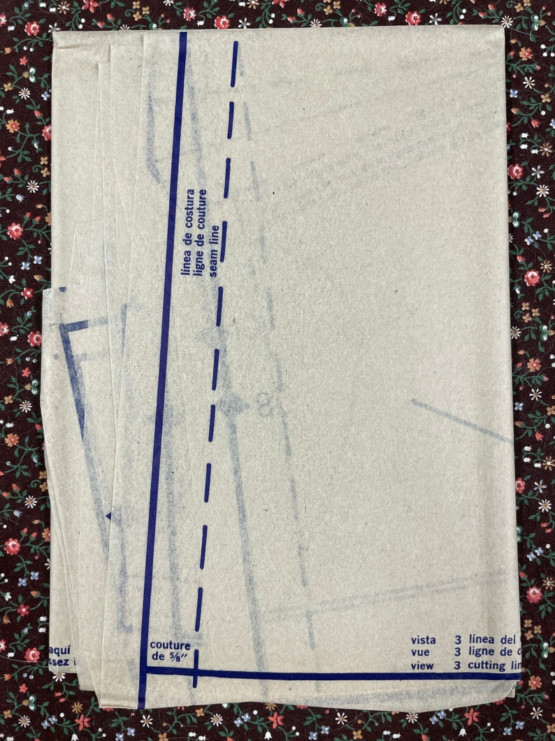 Puede incluir: Una pila de hojas de patr&oacute;n de costura beige con l&iacute;neas azules impresas y texto. El texto incluye "seam line", "couture de 5/8", "vista", "view", "l&iacute;nea del", "ligne de" y "cutting lin".