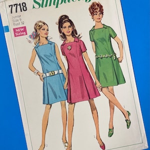 Pode incluir: Padrão de costura Simplicity número 7718 para um vestido júnior tamanho 9 com uma medida de busto de 81 cm. O padrão apresenta três estilos de vestidos diferentes, todos com mangas curtas e uma silhueta simples e de linha A. Os vestidos são mostrados em azul, rosa e verde.