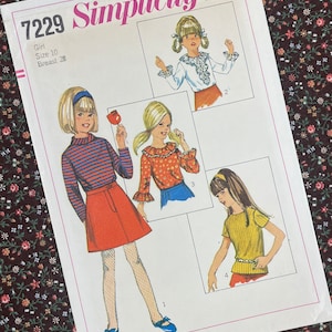 Op de afbeelding: Simplicity naaipatroon nummer 7229 voor een meisjesoutfit. Het patroon bevat vier verschillende stijlen: een shirt met lange mouwen en een geruit kraagje, een shirt met korte mouwen en een geruit kraagje, een gestreept shirt met lange mouwen en een shirt met korte mouwen. Het patroon is voor maat 10 met een borstomvang van 71 cm.