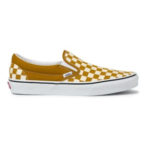 Op de afbeelding: Mosterdgele en wit geruite slip-on sneaker met een witte zool. De schoen heeft een mosterdgele hiel en tong, met het Vans-logo aan de zijkant. De zool heeft een zwarte streep.