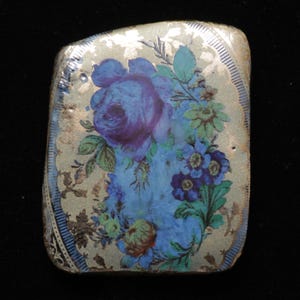 Könnte beinhalten: Eine blaue und goldene Keramikfliese mit einem Blumendesign mit blauen Rosen und anderen Blumen. Die Fliese hat eine strukturierte Oberfläche und einen goldenen Rand.