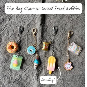 以下が含まれることがあります： Tiny Bag Charms: Sweet Treat Edition。ドーナツ、アイスクリーム、アイスキャンディーなどのチャーム。各チャームは、ロブスタークラスプ付きのチェーンに吊り下げられています。「Drooling!」の文字が画像に表示されています。
