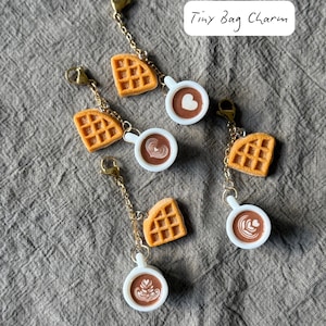 May include: Tiny bag charms featuring miniature waffles and coffee cups with latte art. The charms are connected to gold-colored chains and clasps. The text "Tiny Bag Charm" is written in a white box.