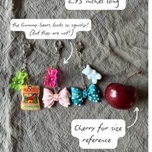 Op de afbeelding: Een verzameling sleutelhangers met gummyberen, strikken en een Haribo snoepverpakking. De sleutelhangers zijn bevestigd aan zilveren sluitingen. De afbeelding bevat een kers ter groottevergelijking. De tekst luidt "the Gummy bears looks so squishy! (But they are not!)".